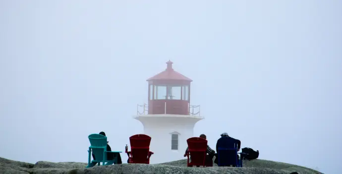 A group of people sitting in lawn chairs in front of a lighthouse